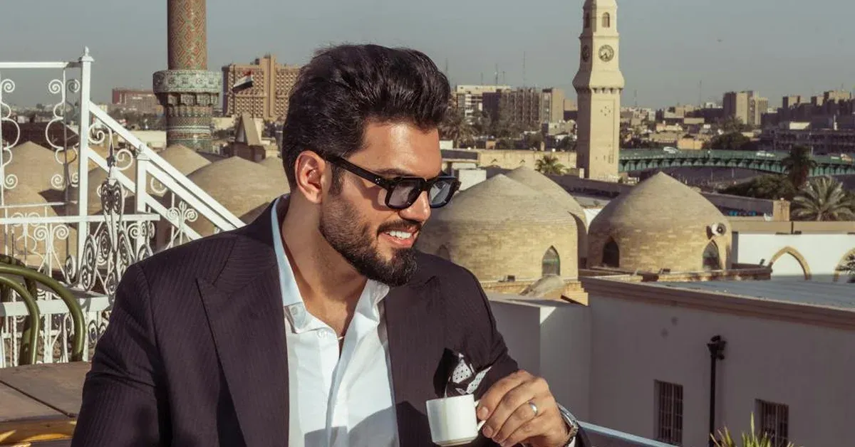 A stylish digital nomad sips coffee on a modern rooftop terrace overlooking the historic cityscape of Baghdad, featuring traditional domes and a clock tower, showcasing Iraq's emerging appeal for remote workers.