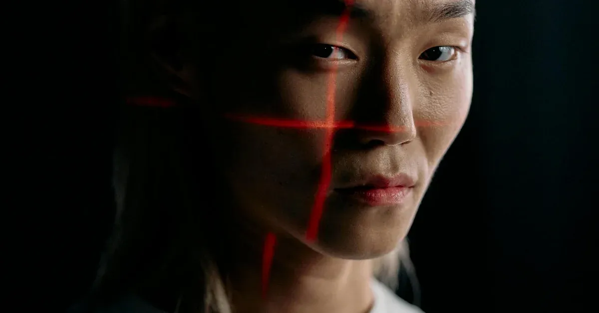 A woman's face is traversed by red laser lines, representing facial recognition scanning, against a dark background, illustrating the impact and scrutiny of AI surveillance.