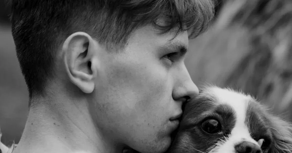 Black and white close-up of a man tenderly kissing his dog on the head, highlighting the deep emotional bond between them.