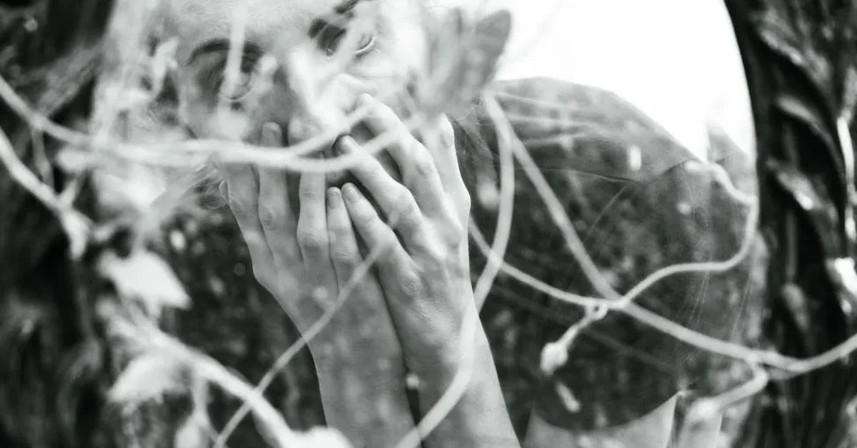Black and white abstract image depicting a figure with hands covering their face, surrounded by swirling lines that evoke complex neural pathways or genetic evolution, symbolizing neurodiversity.