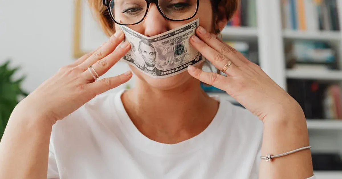 A person holds a five-dollar bill over their mouth, symbolizing the silencing of artistic expression and the influence of wealth in the entertainment industry.